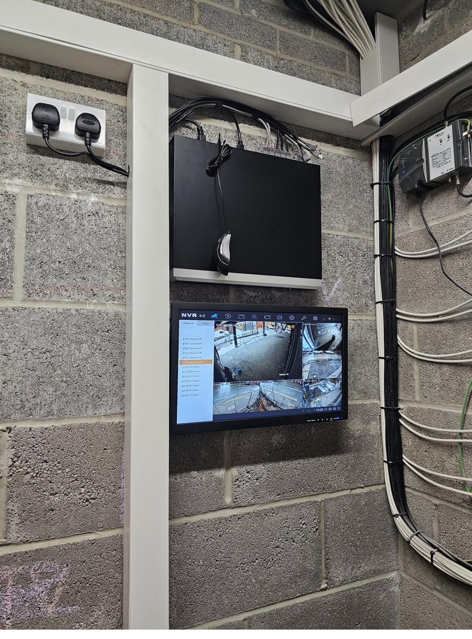 Wall-mounted NVR recorder and monitor showing a live 16-camera grid