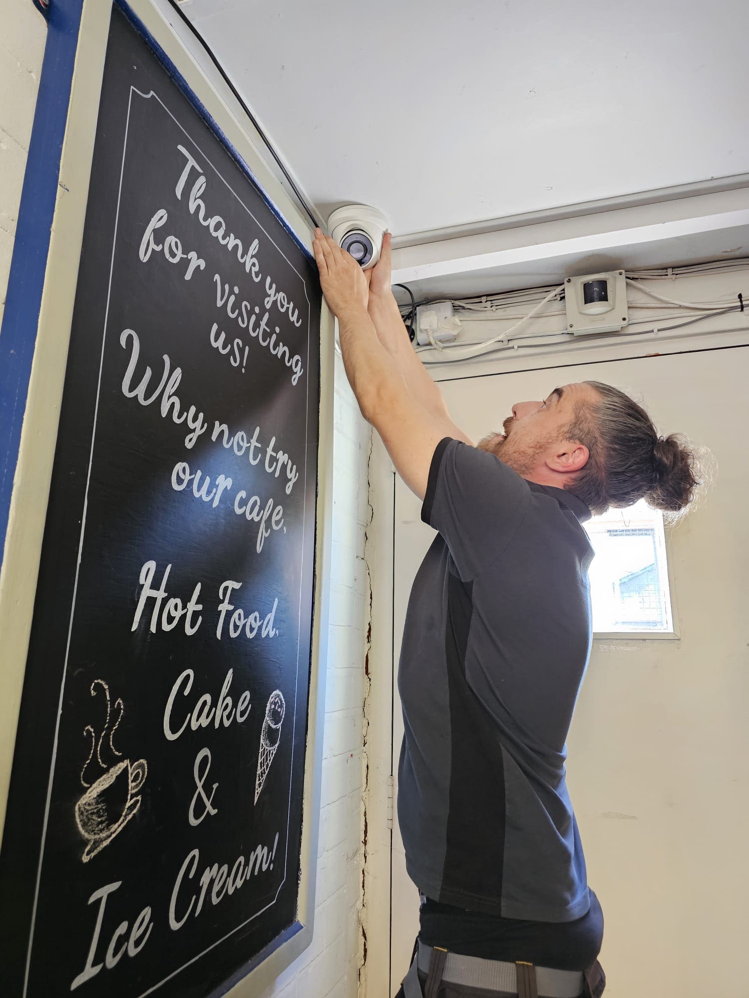 Andy fitting a dome CCTV camera above a café chalkboard in a village shop