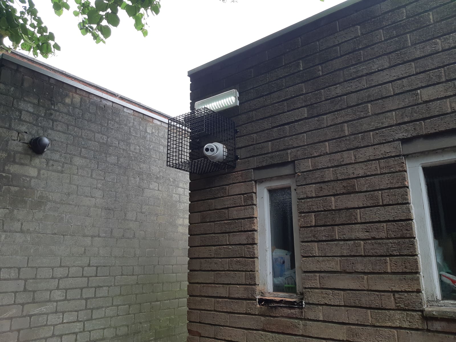 Turret camera and LED floodlight protected by a steel vandal cage on a brick building