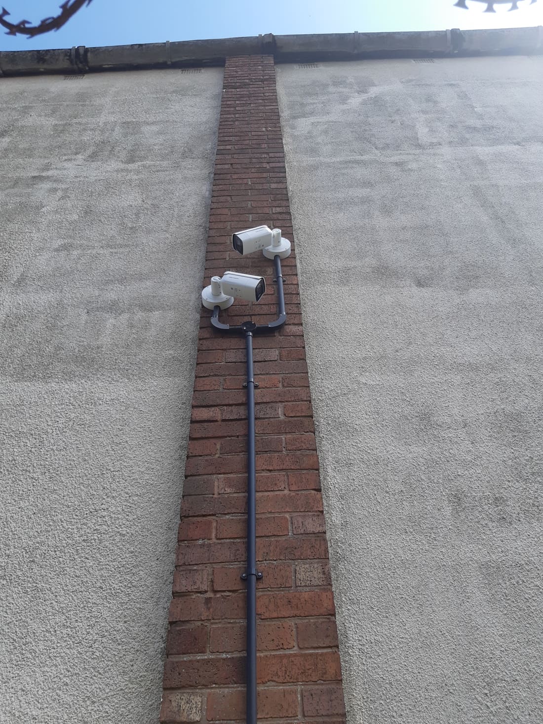 Two bullet cameras mounted back-to-back on a brick chimney stack covering both sides of a property