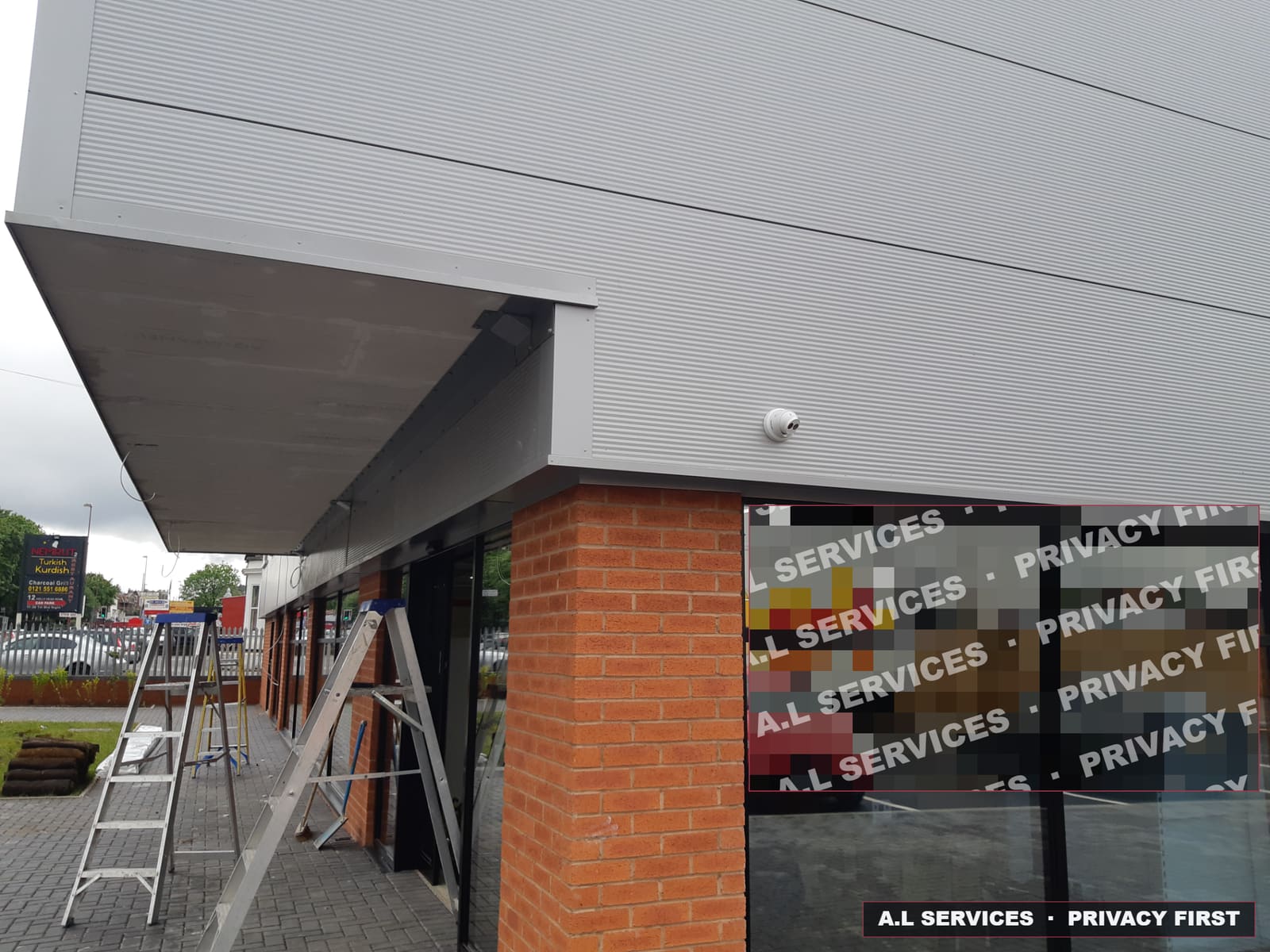 Turret CCTV camera installed under the fascia of a commercial retail unit, interior view pixelated for privacy