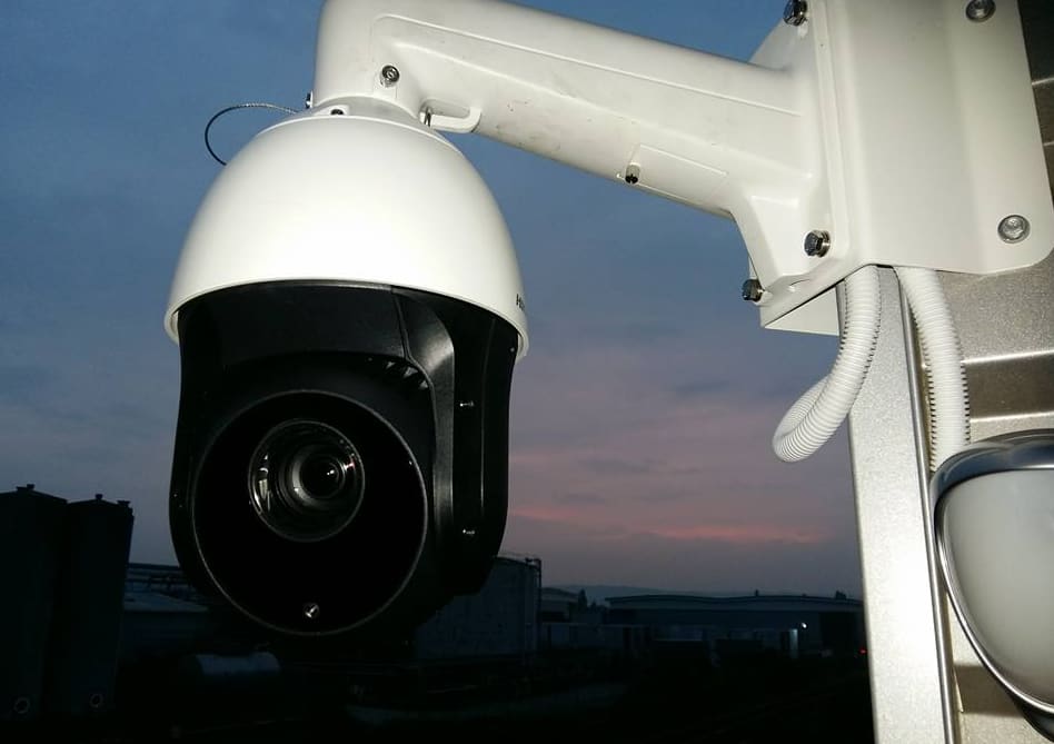 Hikvision PTZ dome camera on a wall bracket at dusk over an industrial yard