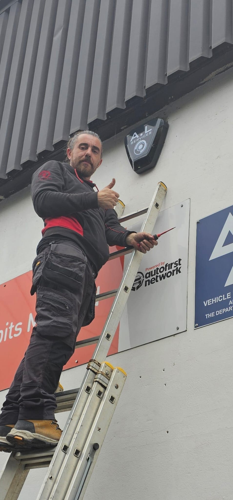 Andy fitting a branded ALServices alarm sounder high on a garage wall