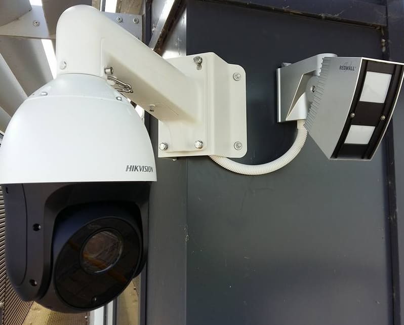 Hikvision PTZ dome camera beside a Redwall long-range detector on a farm building